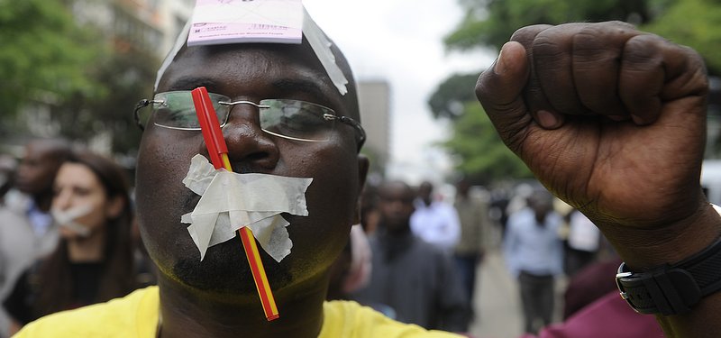 A man with his mouth taped closed raises his fist in protest